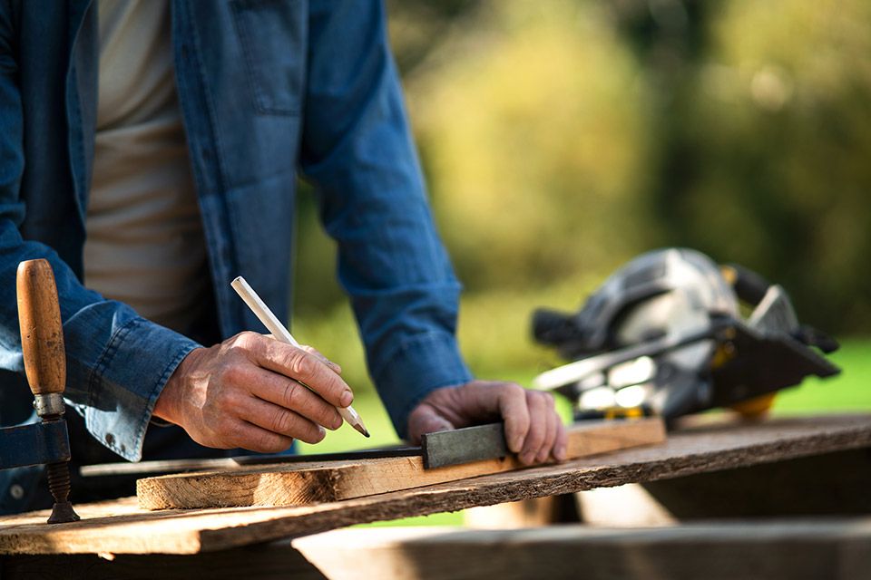 Nahaufnahme eines Handwerkers, der draußen im Garten ein Brett misst.